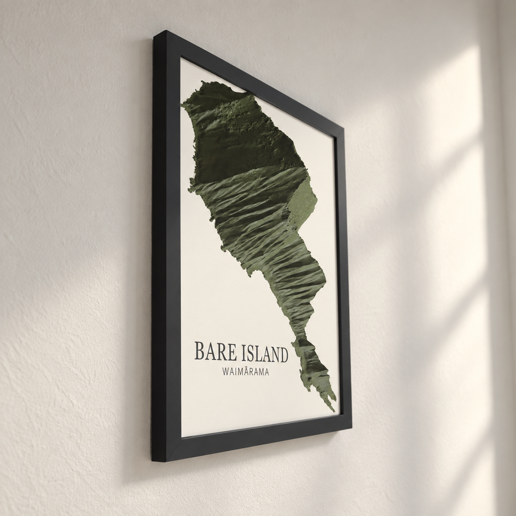 Framed wall art featuring a textured green map silhouette of Bare Island, Waimarama, with the text 'BARE ISLAND' and 'WAIMARAMA' on a white background, shown hanging on a light wall with soft window-light shadows.