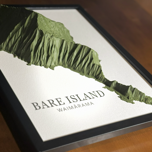 A framed 3D topographic map print of Bare Island, Waimarama, featuring a textured green island design on a white background with a black frame, resting on a wooden surface.